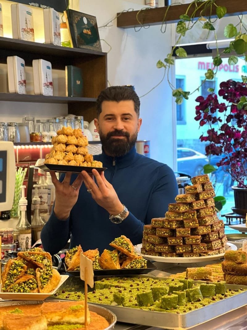 Inhaber Hassan Hayyawi präsentiert ein Tablett Baklava hinter der Theke